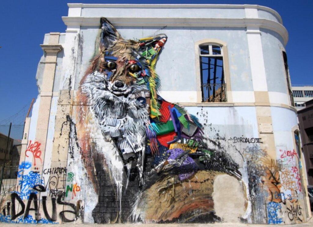 A vibrant street art mural on a weathered building depicts a colorful fox made of geometric shapes, channeling the creativity of renowned street artists. The fox is detailed with shades of red, blue, green, and yellow. Surrounding it are graffiti tags against the backdrop of broken windows.
