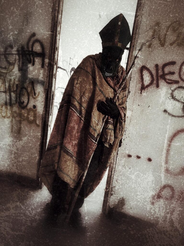 A figure in a mitre hat and ornate cloak holds a staff, standing in a rundown, graffitied room with faded walls—a haunting scene for a Gothic Multimedia Project. The shadowed face adds to the mysterious atmosphere as light enters from the left.