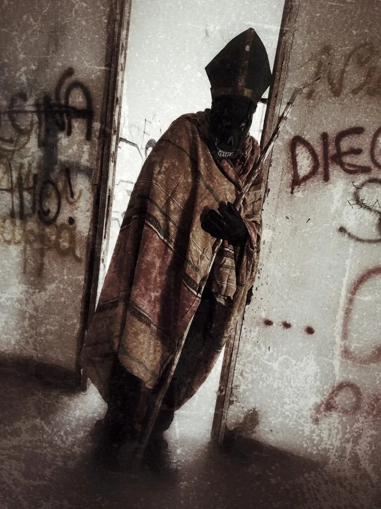 A figure in a mitre hat and ornate cloak holds a staff, standing in a rundown, graffitied room with faded walls—a haunting scene for a Gothic Multimedia Project. The shadowed face adds to the mysterious atmosphere as light enters from the left.